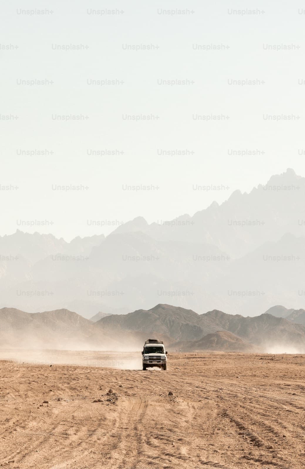A truck driving through a desert with mountains in the background